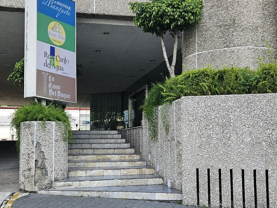 Escalera de piedra de la entrada de personas del hotel, con el tótem que anuncia La Boutique del Banquete, Kon Tiki, Real Canto del Agua y La Cava del Duque